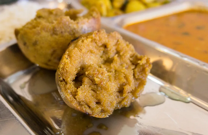 स्टील की थाली में दो सुनहरे बाफले और पीछे दाल